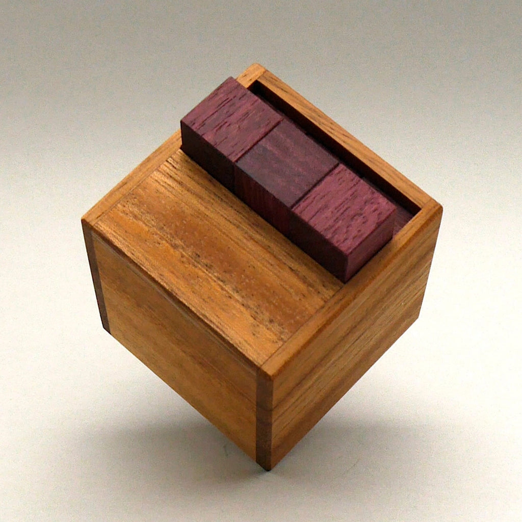Geschlossene Holzbox mit eingesetzten roten Bausteinen als anspruchsvolles Holzpuzzle für Tüftler und Knobelfans.