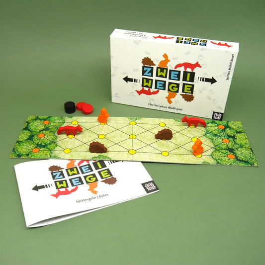 Komplettansicht des Taktikspiels „Zwei Wege“ mit Schachtel, Regelheft, Spielfeld und hölzernen Tierfiguren auf grünem Tisch.