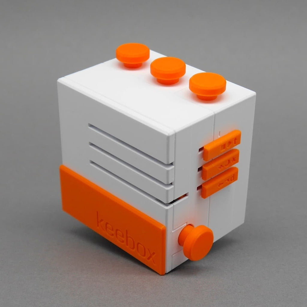 Keebox orange 3D-Puzzle: weiße Knobelbox mit orangefarbenen Reglern und Knopf auf grauem Hintergrund.