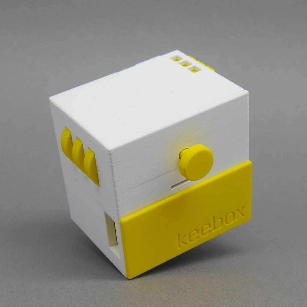 Weiße und gelbe Keebox als braingame-Würfel; Vorderseite mit rundem Drehknopf und gelber Klappe