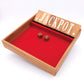 Das Holzspiel Shut the box mit rotem Flies ausgekleidet und zwei Würfeln. Die Klappen sind hochgestellt.