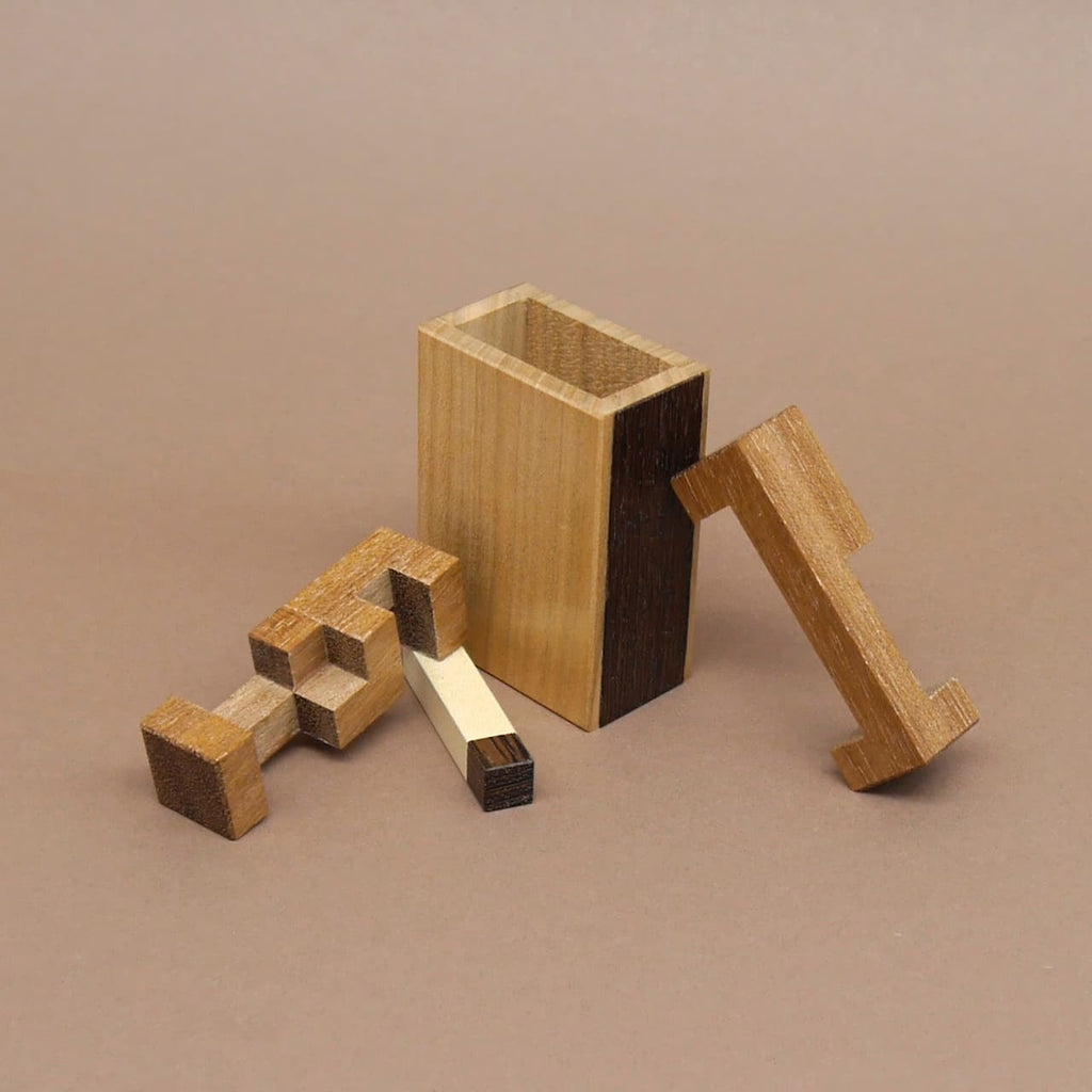 Zerlegtes Holzpuzzle bestehend aus einer rechteckigen Hülle und mehreren geometrisch geformten Einzelteilen aus verschiedenfarbigem Holz.