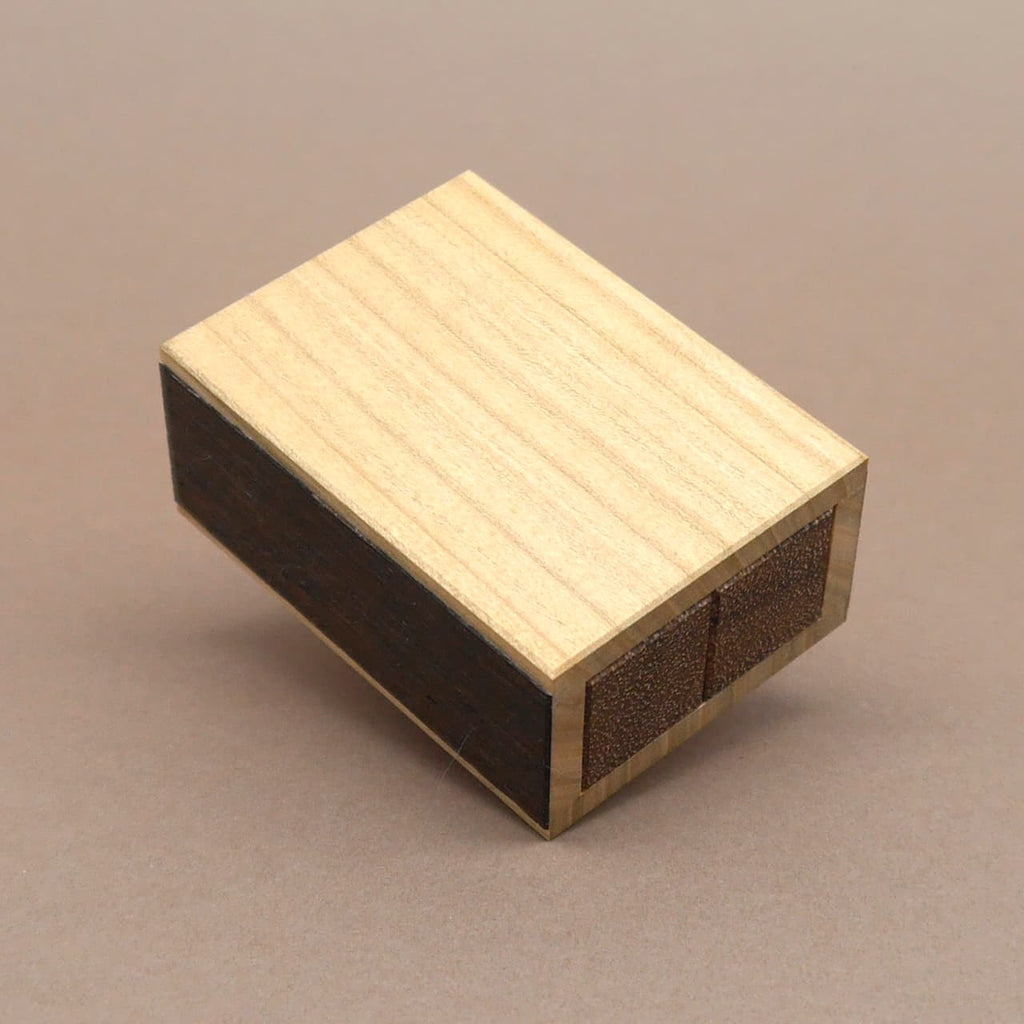 Verschlossenes Holzpuzzle in Form einer kompakten, rechteckigen Schachtel mit glatter Oberfläche aus hellem und dunklem Holz.
