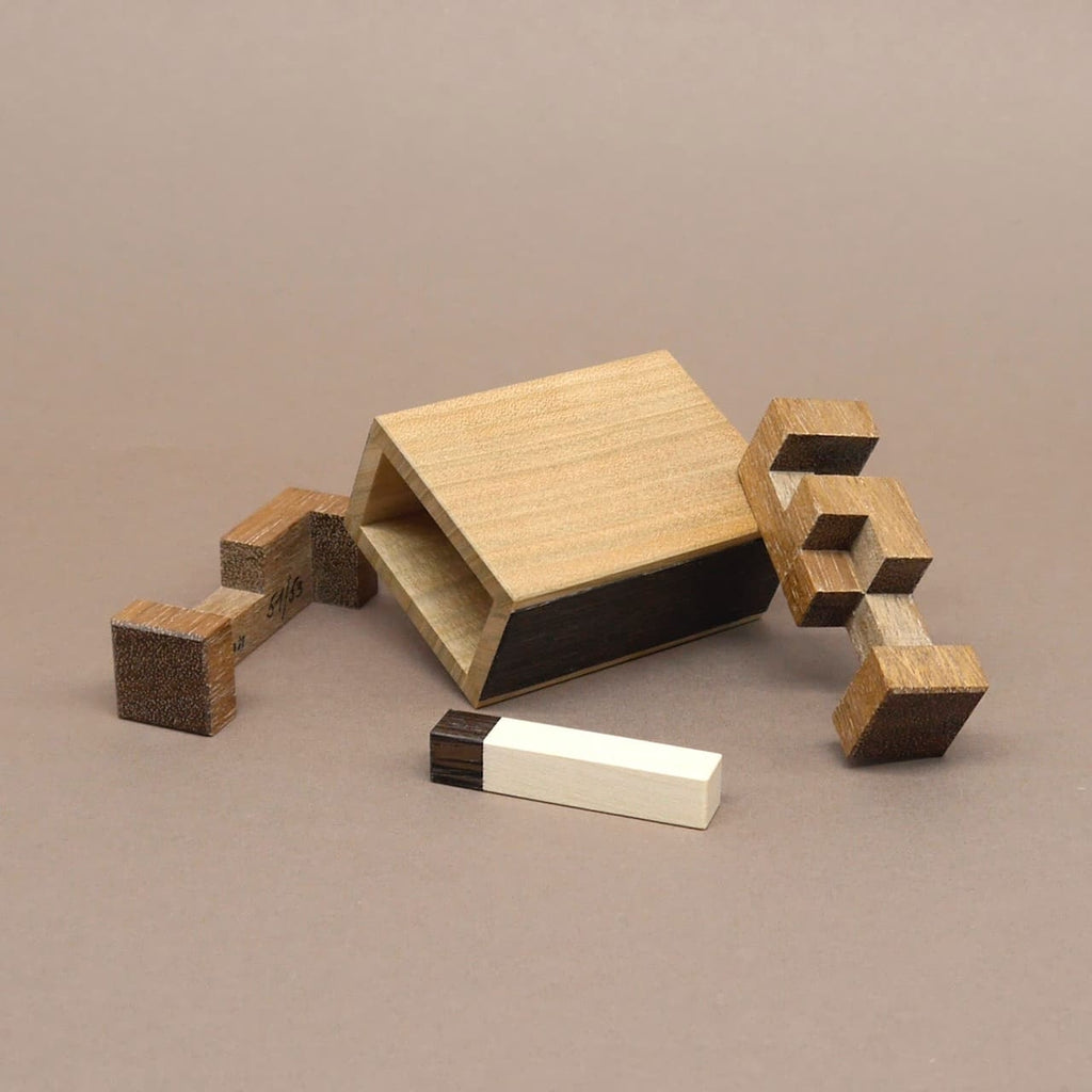 Geöffnetes Holzpuzzle mit fünf auseinandergelegten Teilen, die aus verschiedenfarbigem Holz gefertigt und geometrisch ineinander steckbar sind.