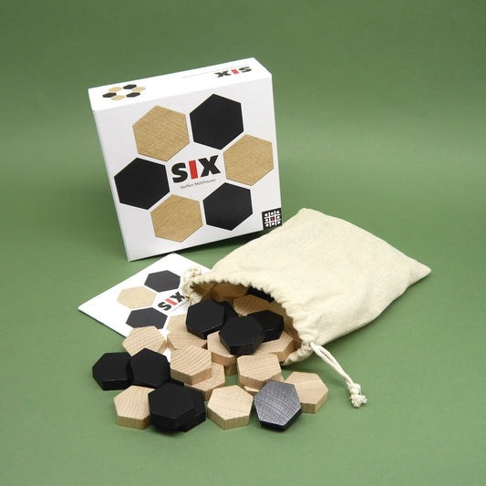Schachtel und Beutel des taktikspiel „SIX“; zahlreiche schwarze und naturfarbene Hexagon-Steine sind ausgestreut.